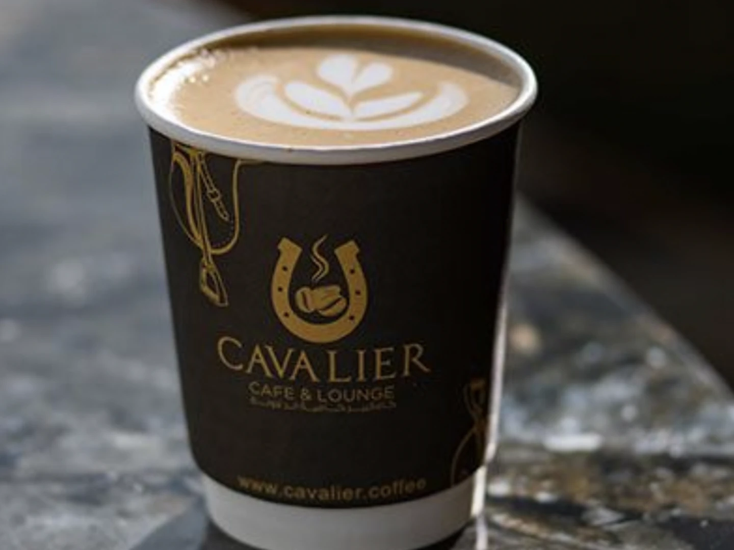 Cavalier Cafe cappuccino in a black branded cup with palm-leaf latte art, Doha specialty coffee